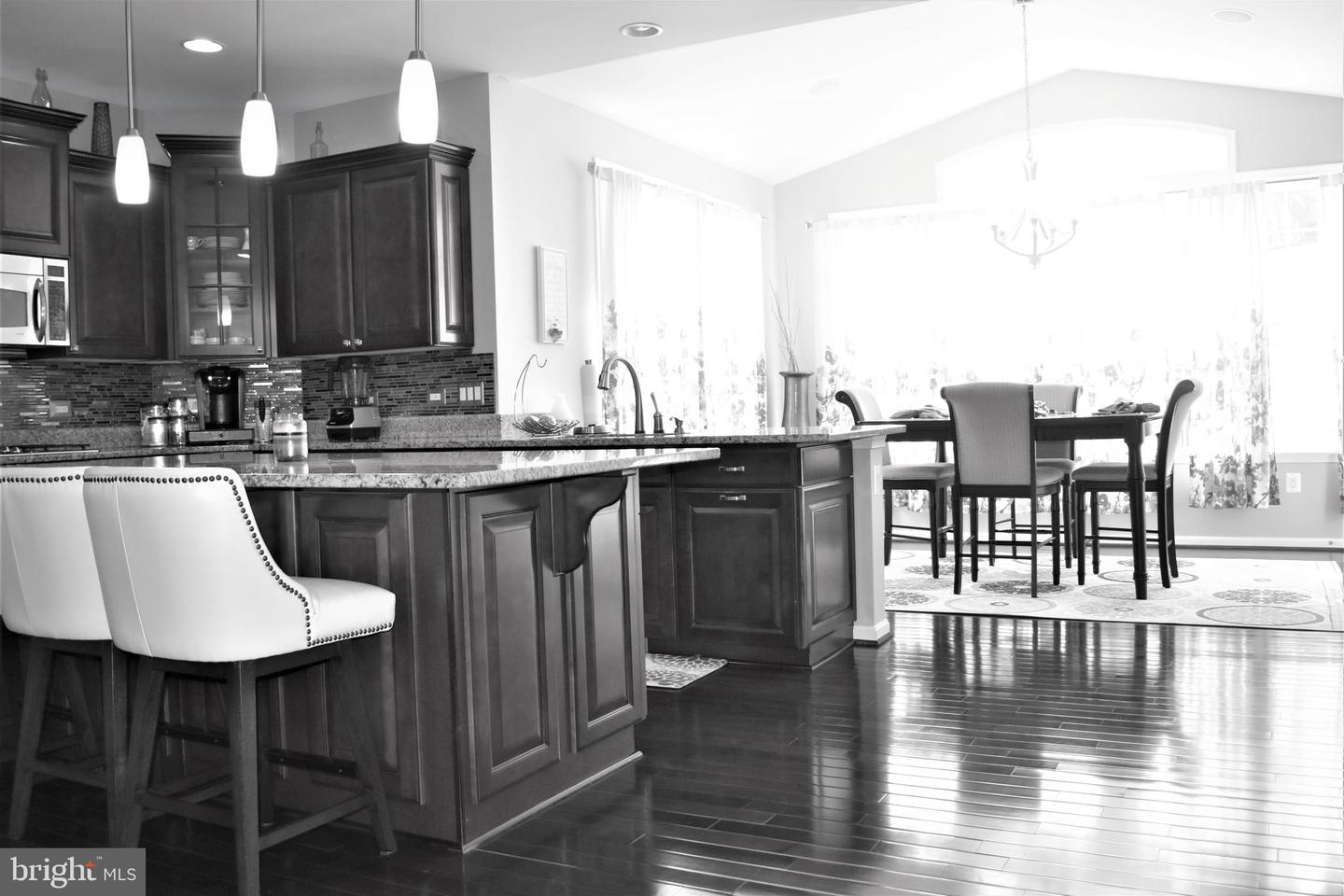 Kitchen with dark wood cabinets and granite counters opening to a dining area with large windows.