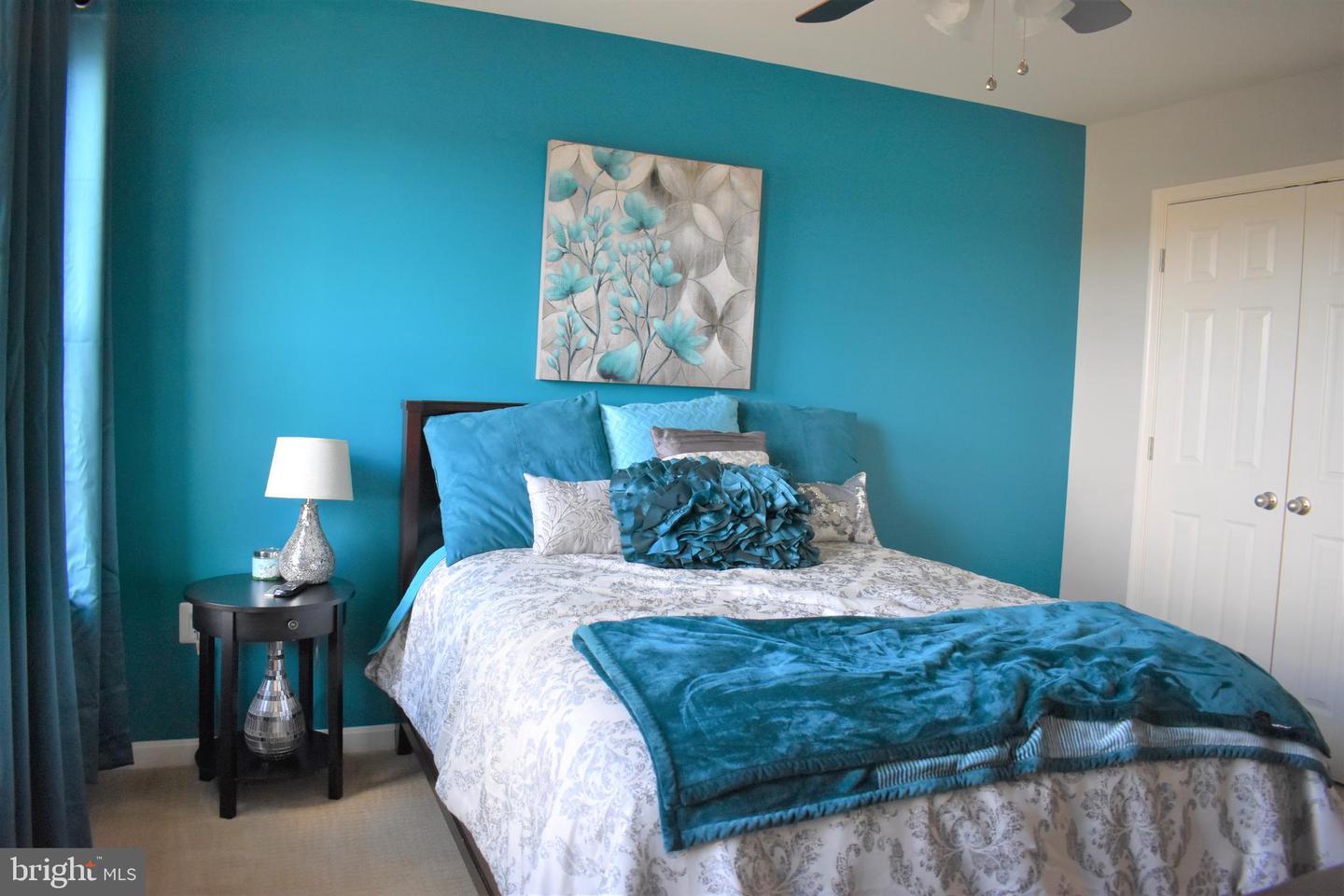 Staged bedroom with a turquoise accent wall, teal bedding, floral artwork, and white double closet doors.