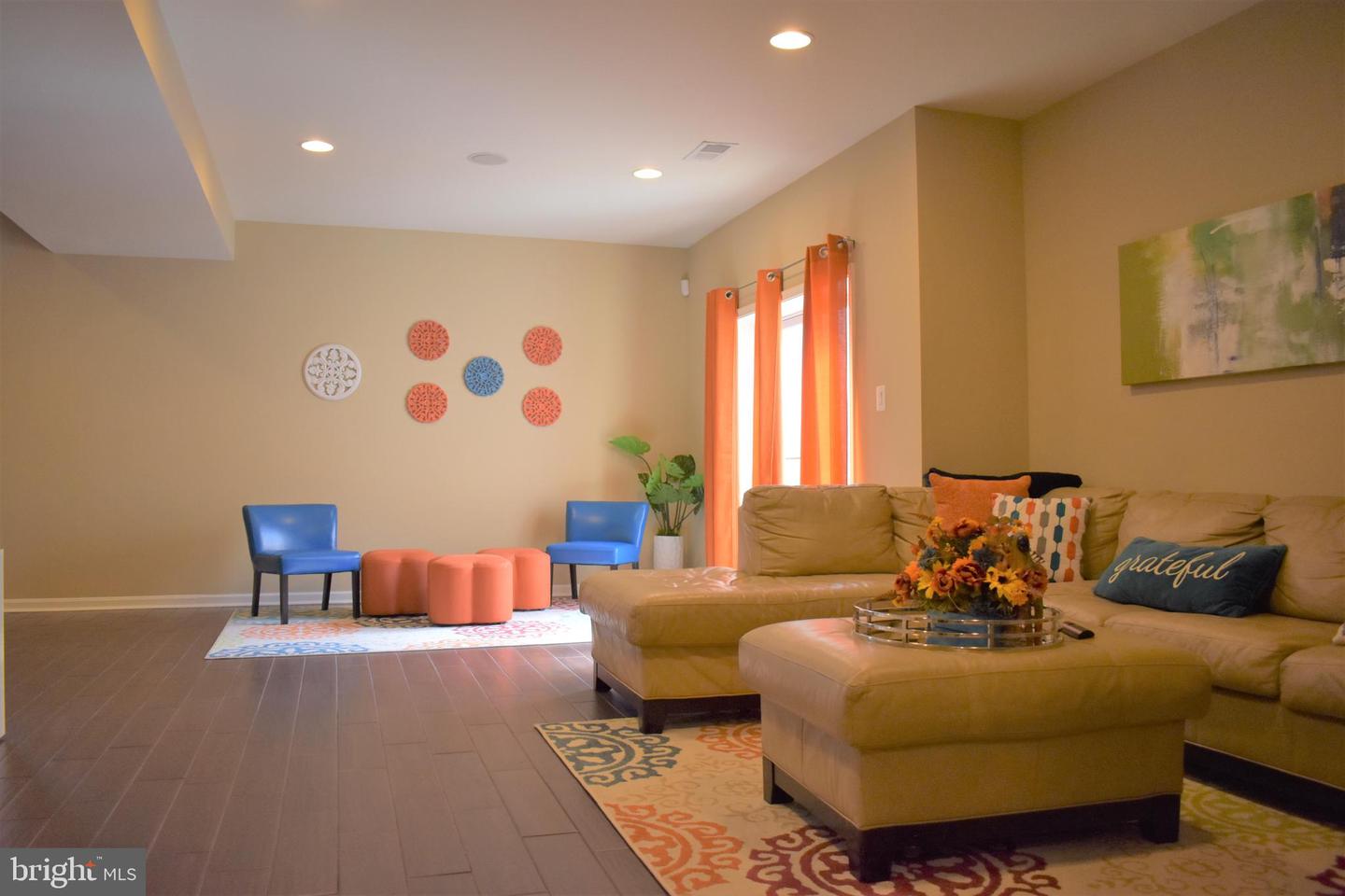 Living room with a tan sectional, blue chairs, coral ottomans, and orange curtains.