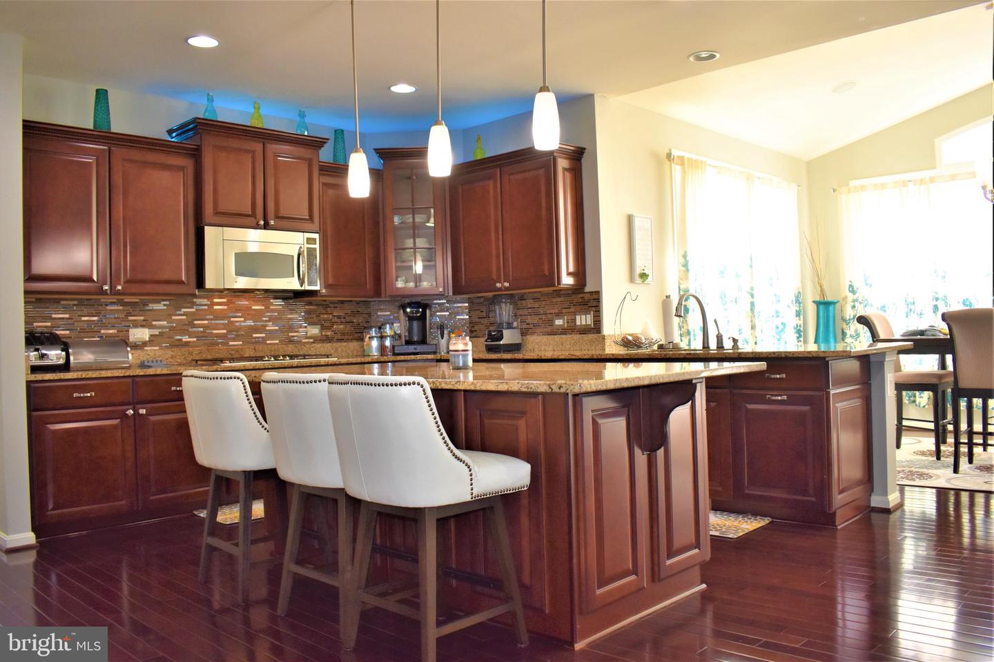 Kitchen with cherry cabinets, granite island, pendant lights, and white bar stools.