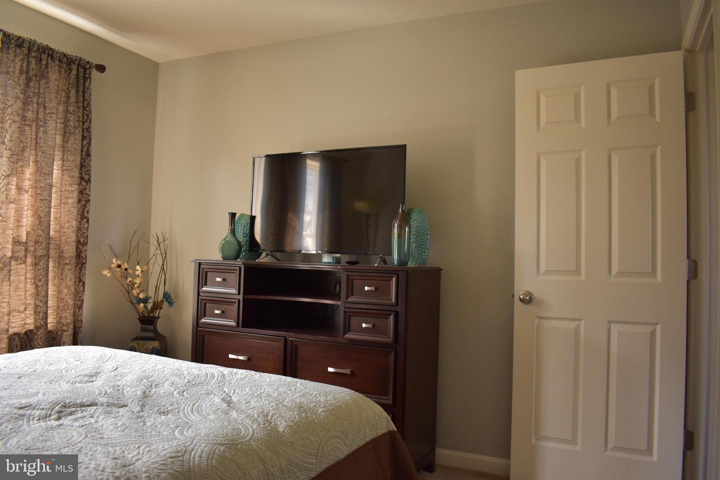 Bedroom with a white quilted bed, dark wood TV dresser, and patterned curtains.