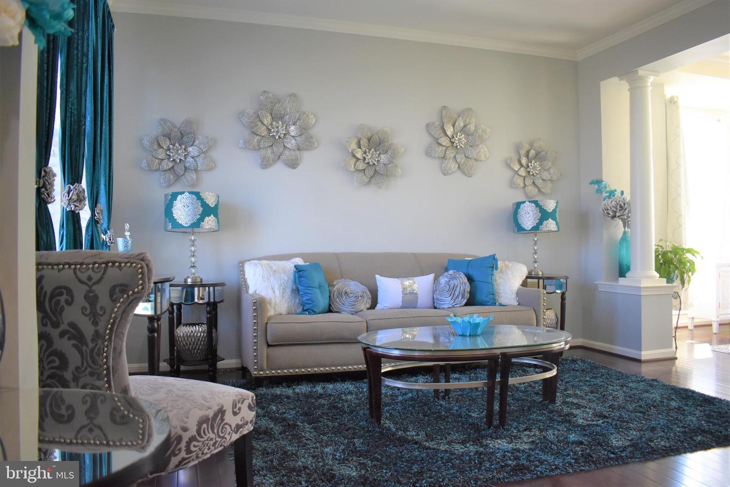 Living room with a gray sofa, turquoise accents, silver flower wall decor, and a glass coffee table.