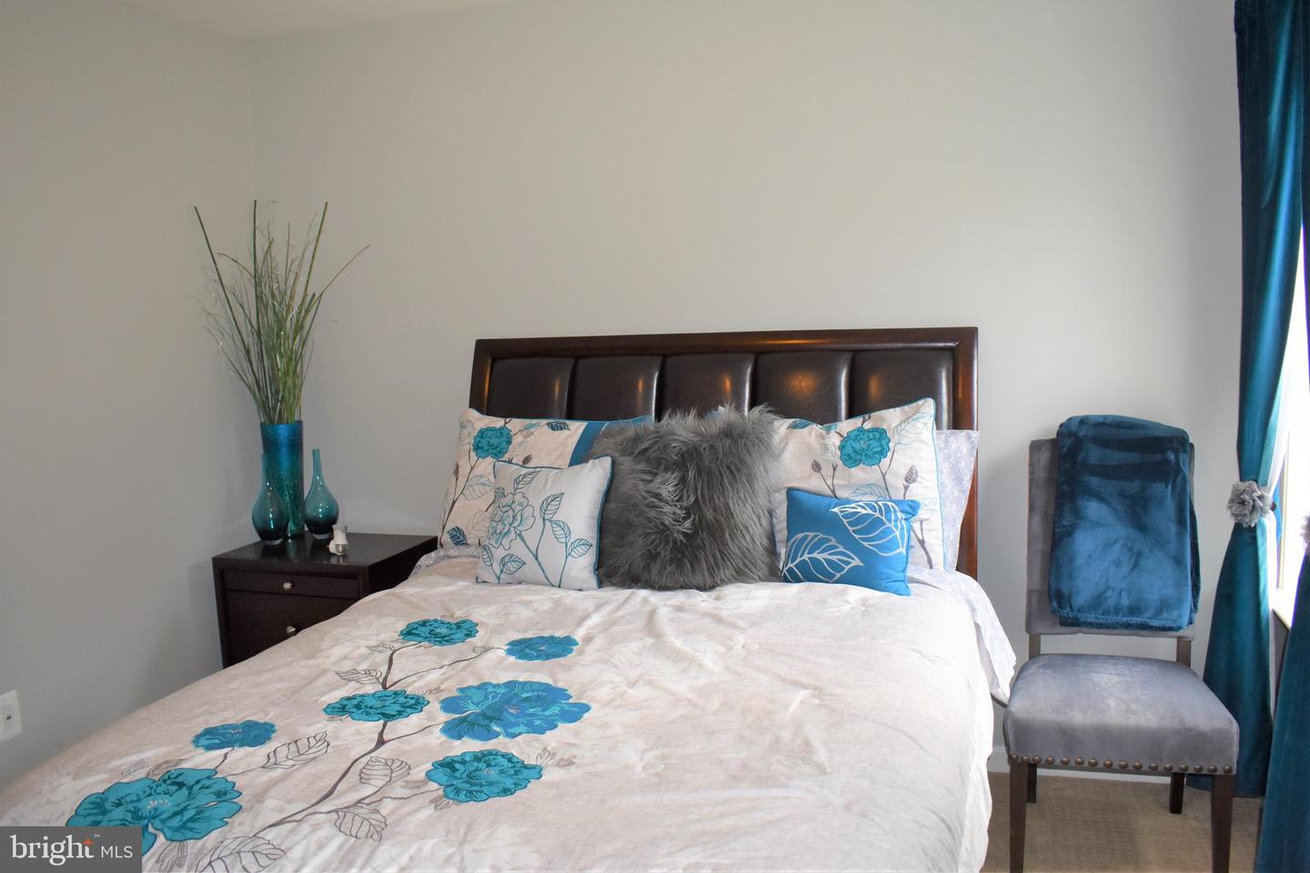 Bedroom with teal floral bedding, a dark wood headboard, and an upholstered chair by the window.