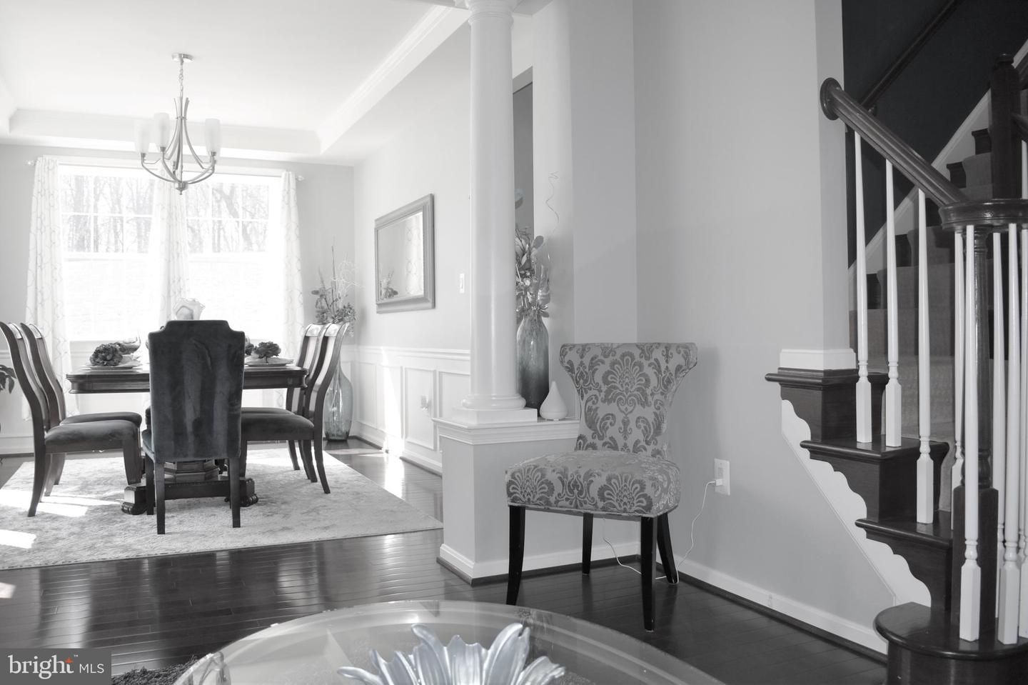 Staged dining area with a dark wood table beside a staircase and patterned accent chair.