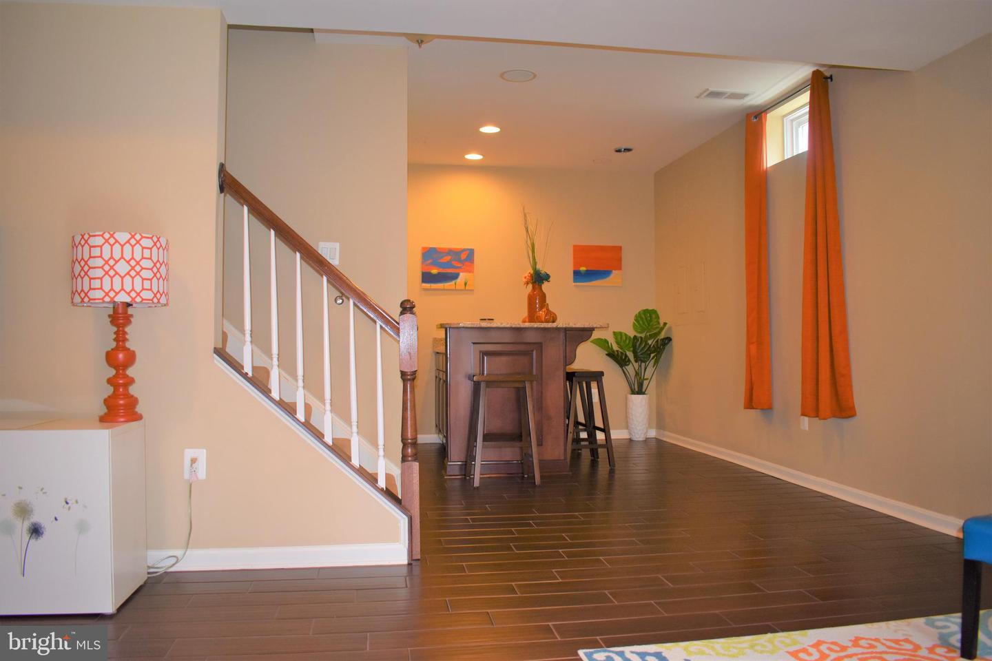 Furnished interior with a staircase, dark tile flooring, and a compact bar beneath colorful artwork.