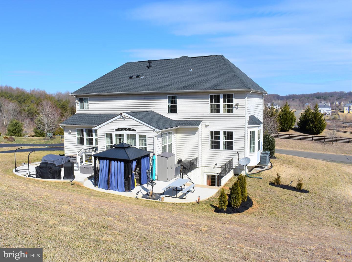 Rear of a two-story white house with a patio, curtained gazebo, and dormant lawn.