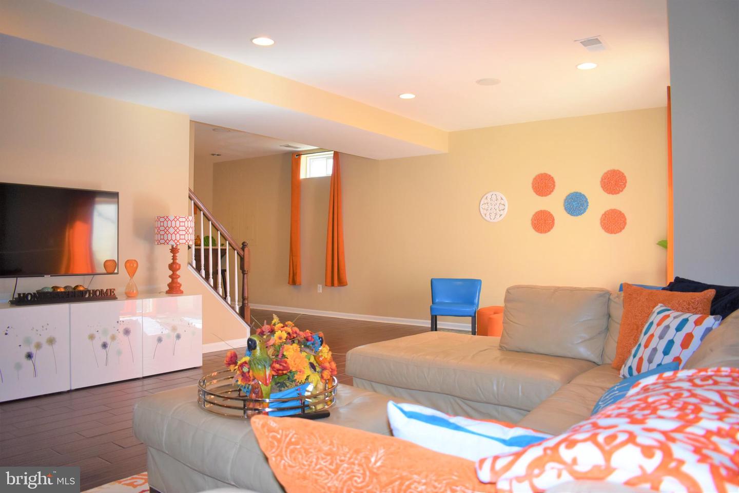 Furnished living room with a beige sectional, colorful accents, and a staircase.