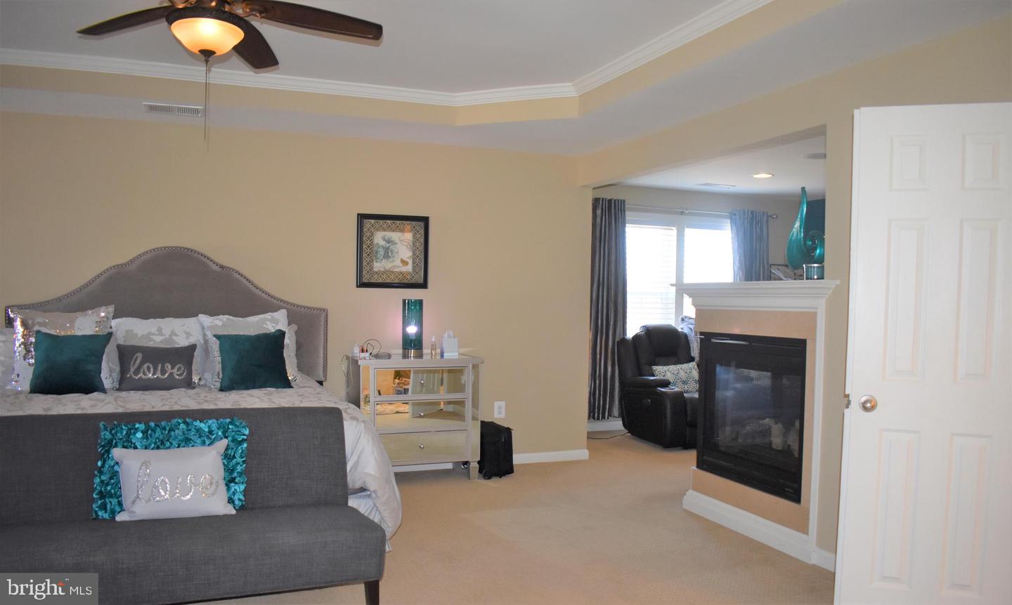 Bedroom with a gray upholstered bed, teal pillows, and a fireplace beside a sitting area.