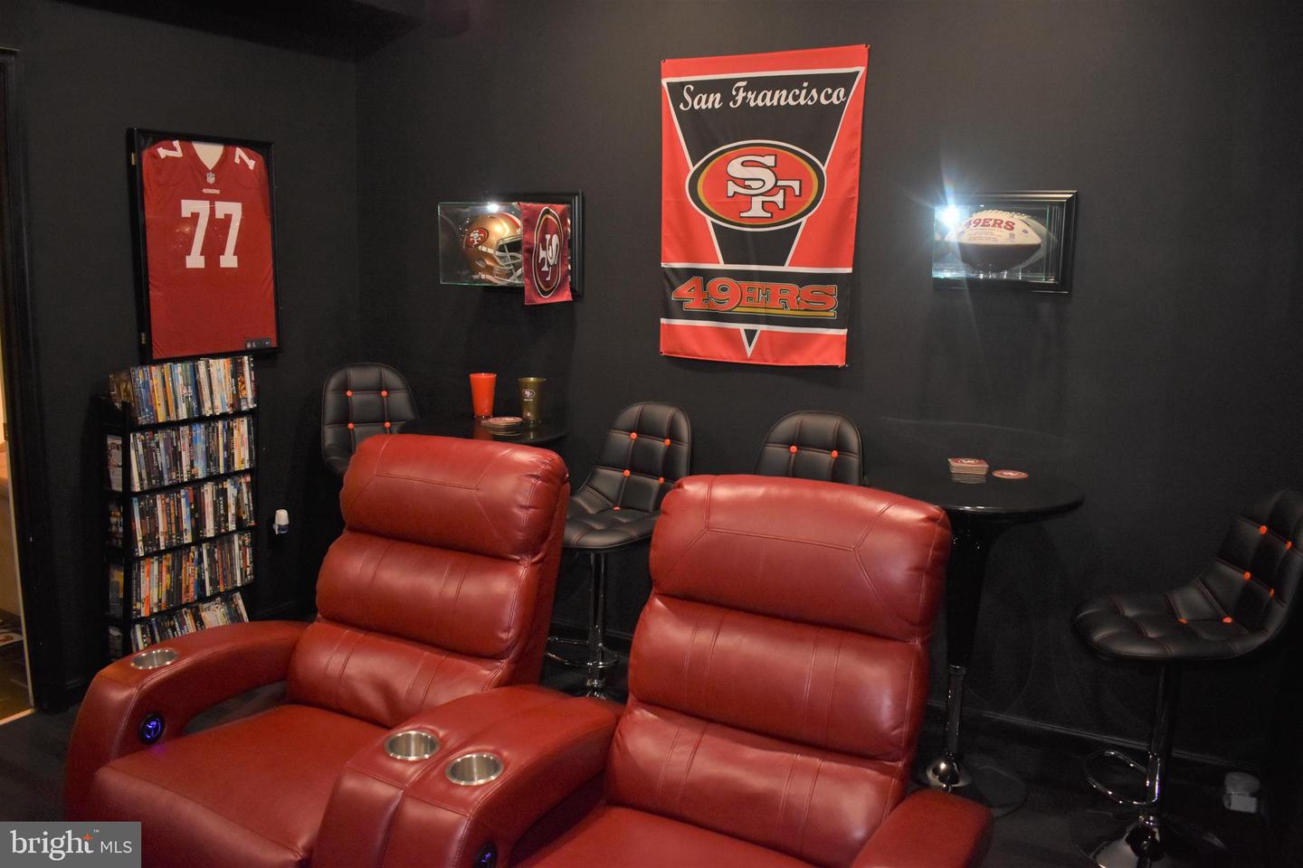Home theater with red leather recliners, black walls, and San Francisco 49ers memorabilia.