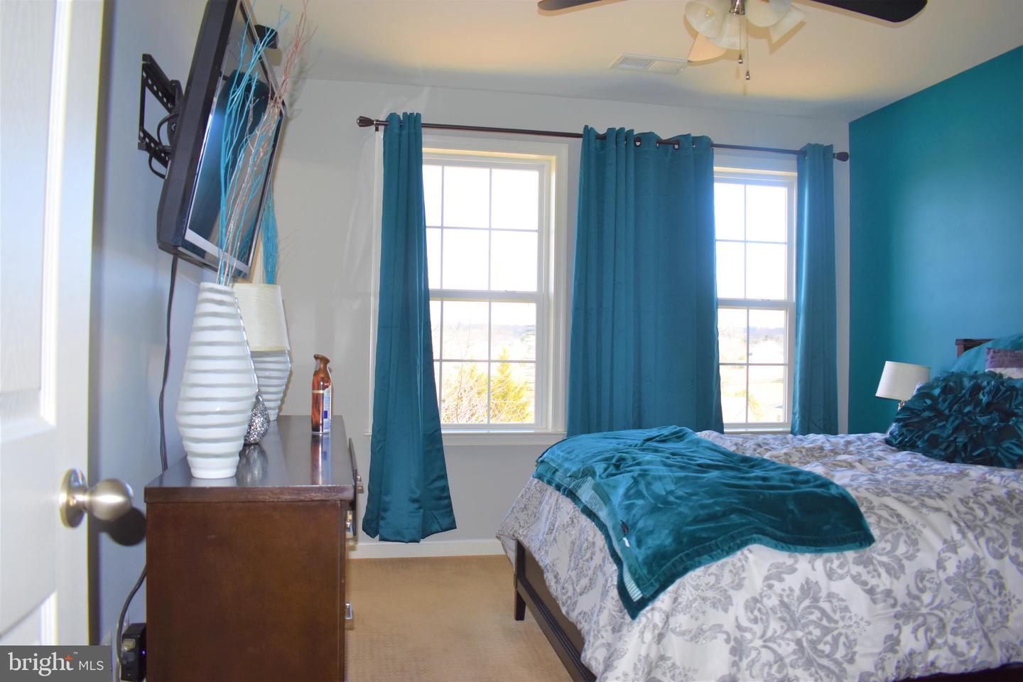 Bedroom with teal curtains and accent wall, patterned bedding, and two windows.