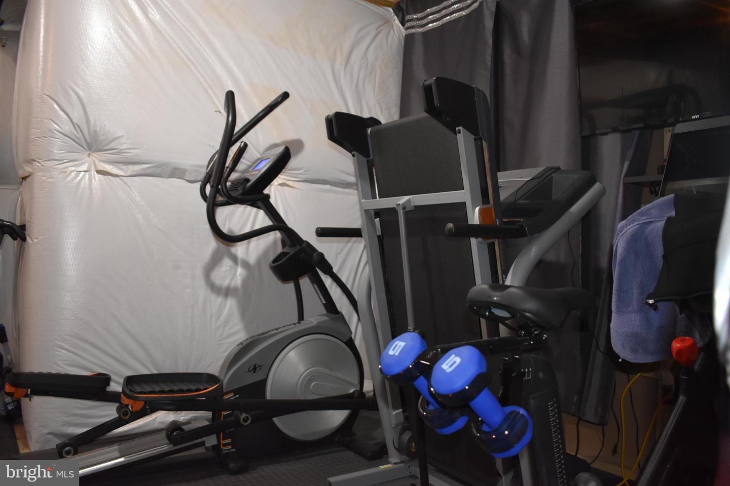 Home gym with an elliptical, weight machine, stepper, and blue dumbbells.