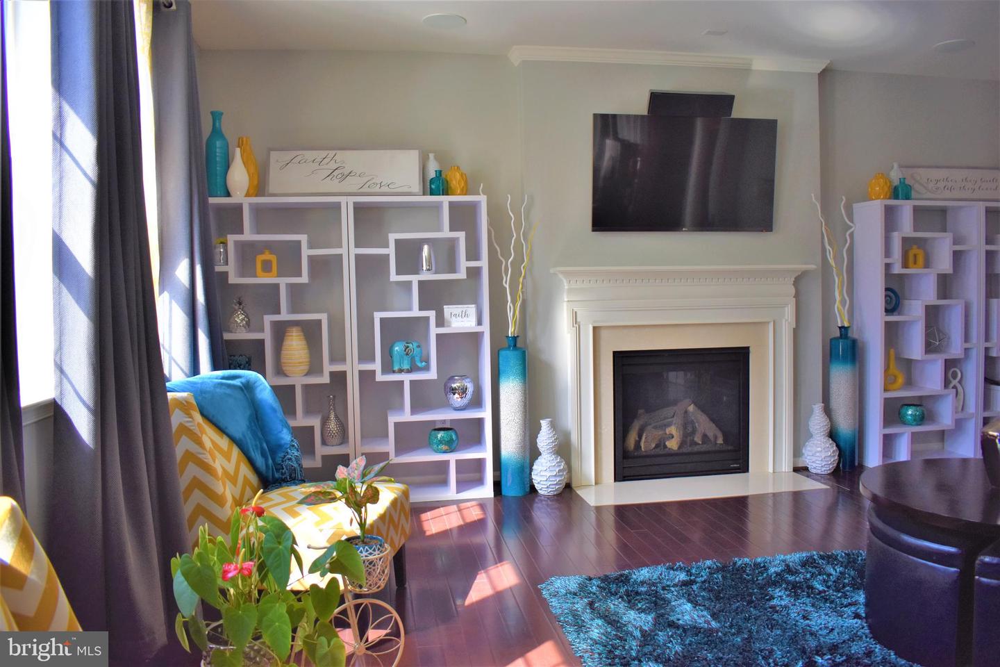 Living room with a white fireplace, wall-mounted TV, display shelves, and blue accents.