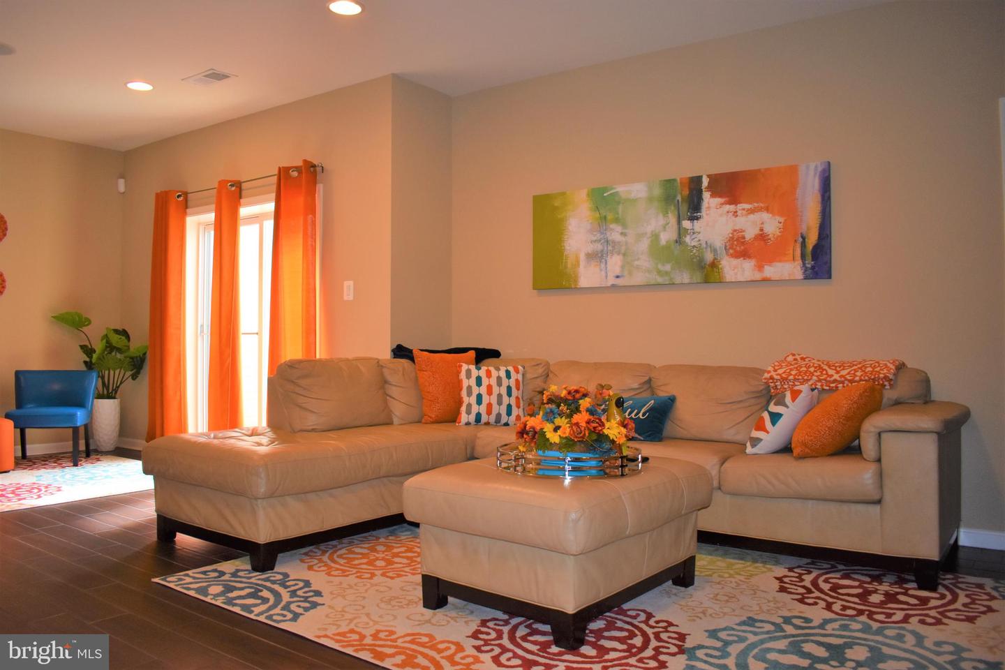 Living room with a beige sectional, colorful rugs and cushions, and orange curtains by a sliding glass door.