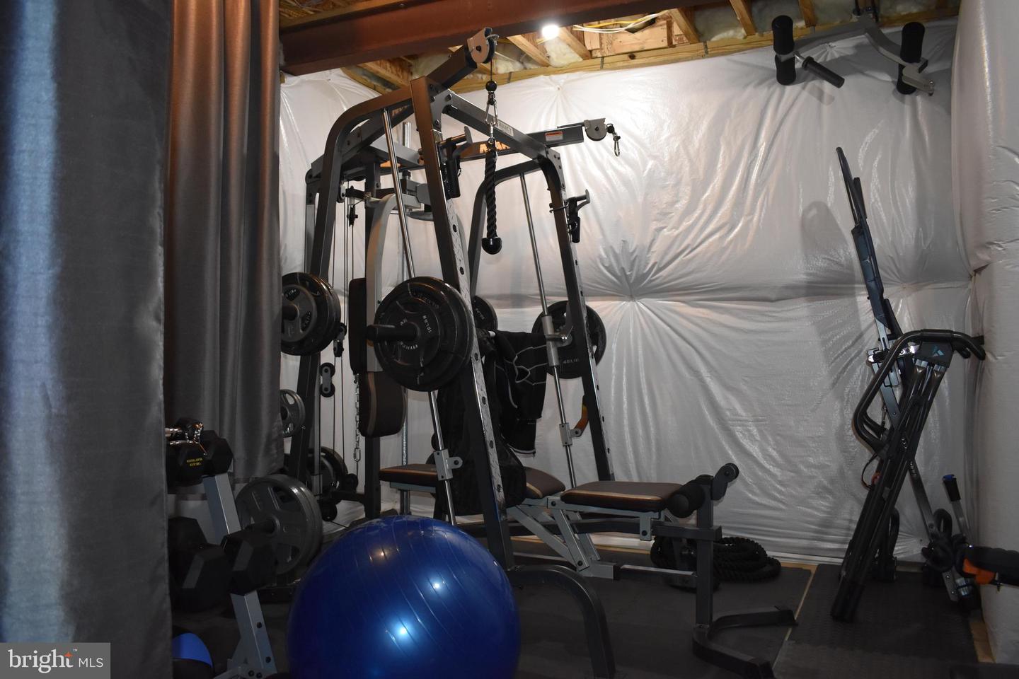 Basement gym with a multi-station weight machine, bench, cardio equipment, and blue exercise ball.