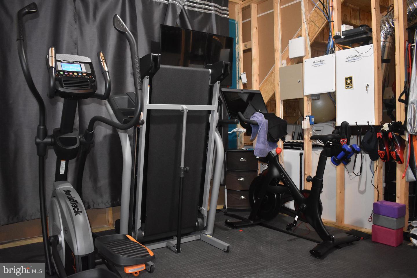 Basement home gym with exercise machines, dumbbells, and exposed wall framing.