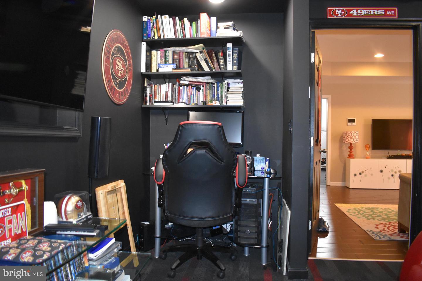Home office with dark walls, a gaming chair, book-filled shelves, and San Francisco 49ers memorabilia.