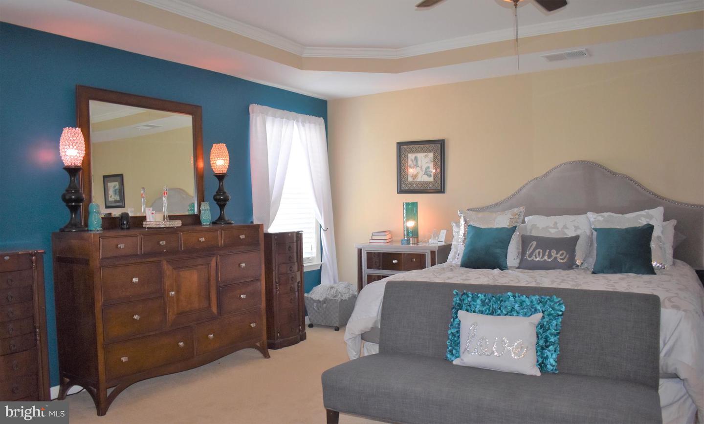 Furnished bedroom with a teal accent wall, carved wooden dresser, and gray bench at the foot of the bed.