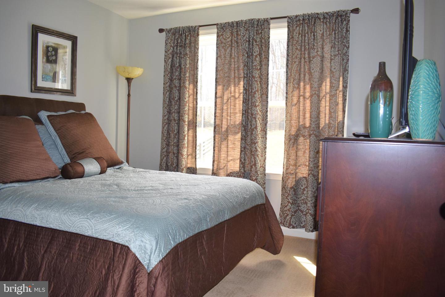 Furnished bedroom with a large bed, patterned curtains, and a wooden dresser.