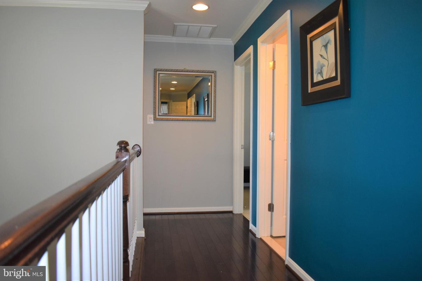 Upstairs hallway with dark hardwood floors, white balusters, teal accent wall, and framed mirror.