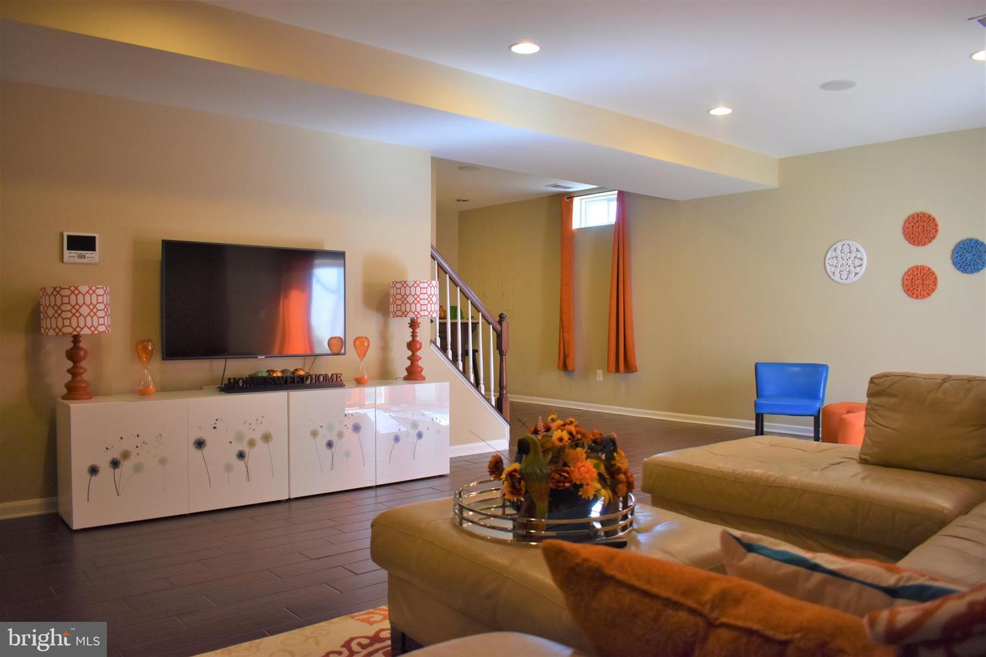 Living room with tan sectional, floral media cabinet, wall-mounted TV, and staircase.
