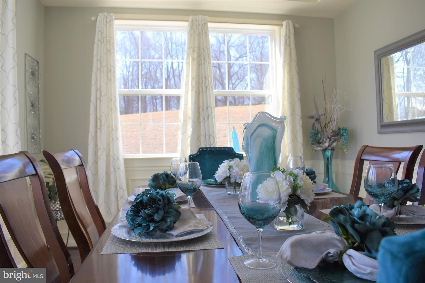 Dining room with a polished table, teal-and-white floral decor, and large curtained windows.
