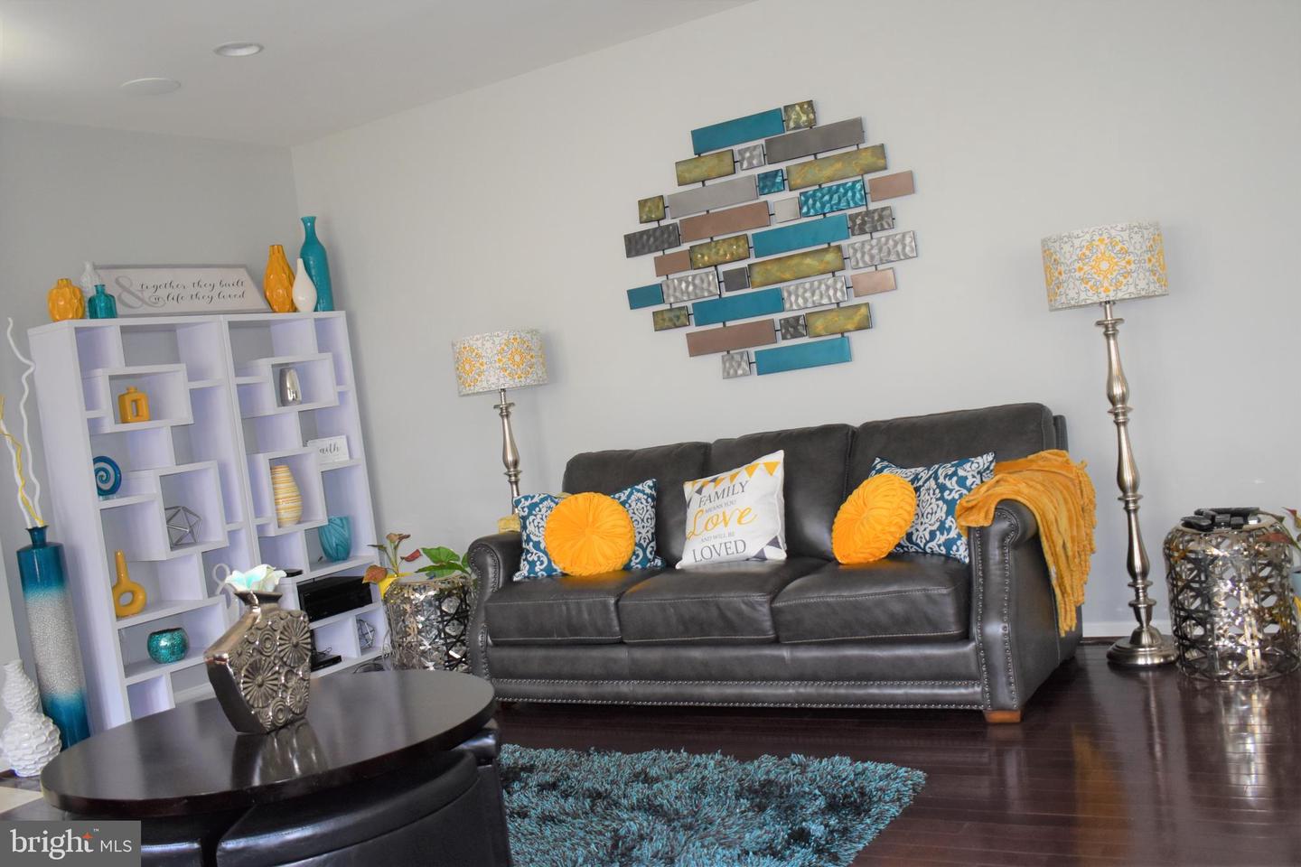 Living room with a dark leather sofa, orange accent pillows, turquoise rug, and colorful geometric wall art.