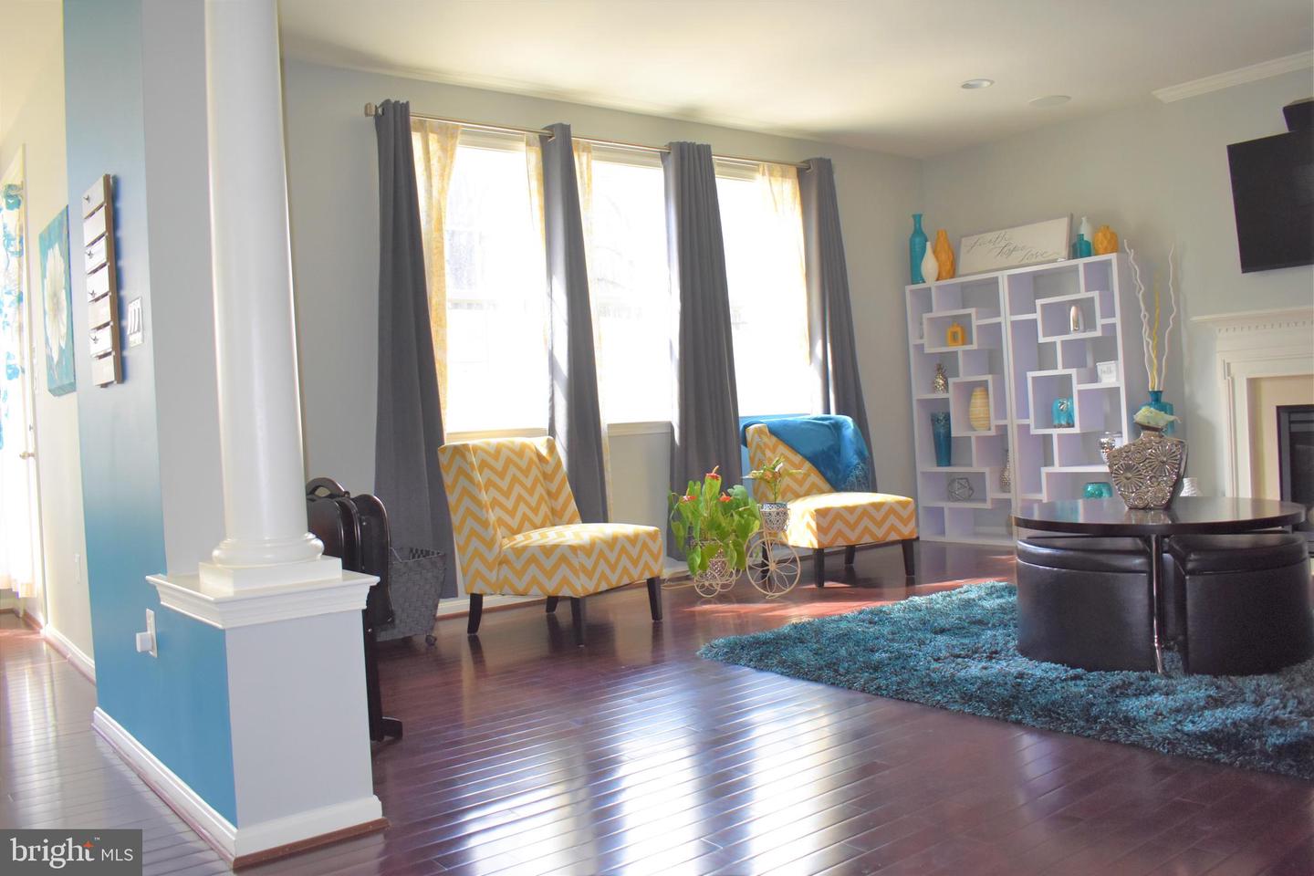 Living room with tall curtained windows, yellow chevron chairs, dark hardwood floors, and a turquoise rug.