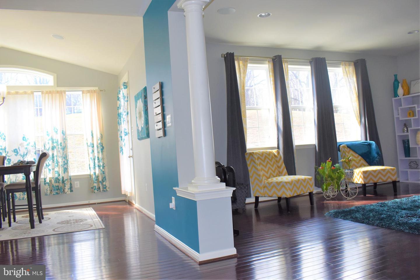 Open living and dining area with dark hardwood floors, teal accent wall, and yellow chevron armchairs.