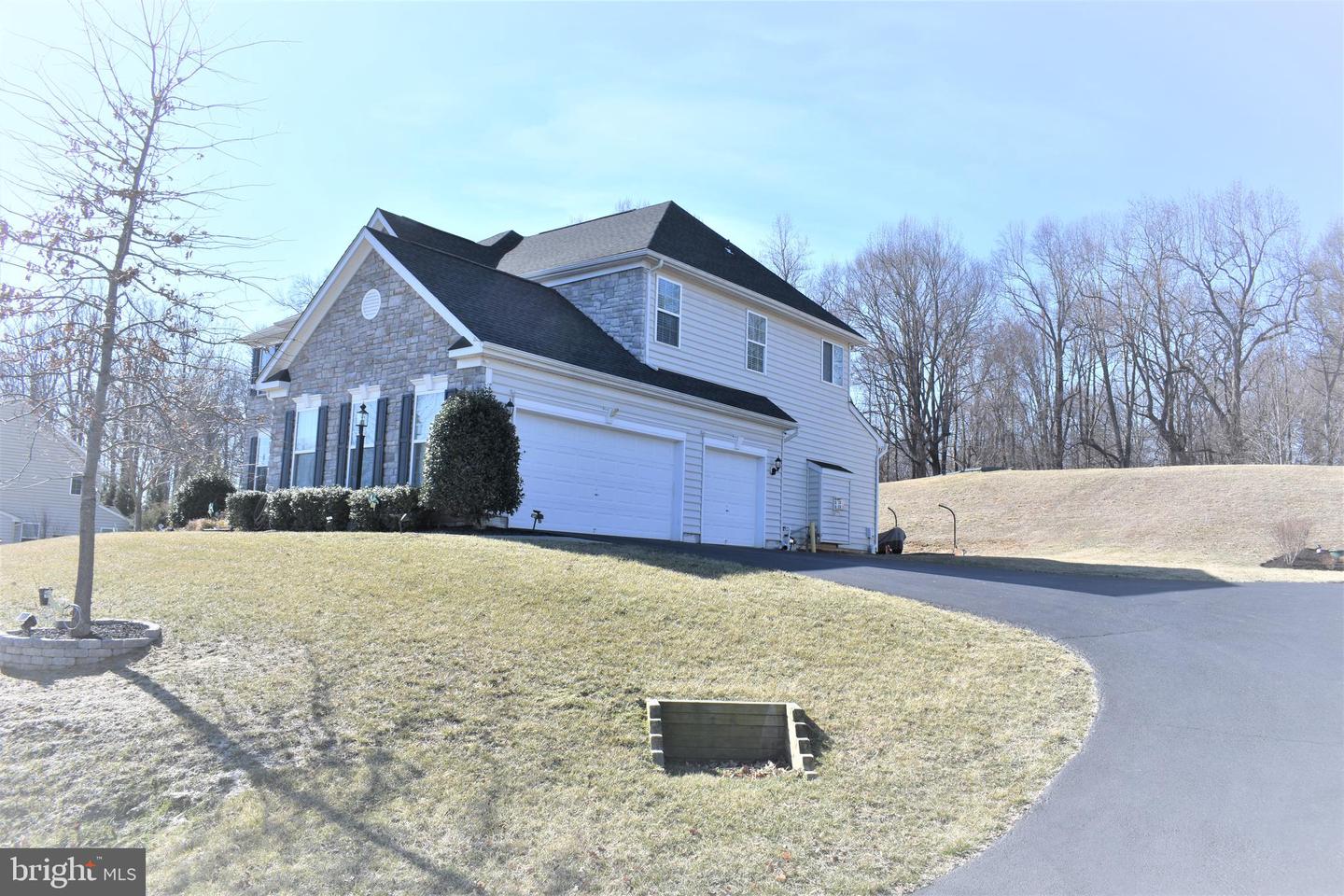 Two-story house with a stone facade, white siding, and double garage beside a curved driveway.