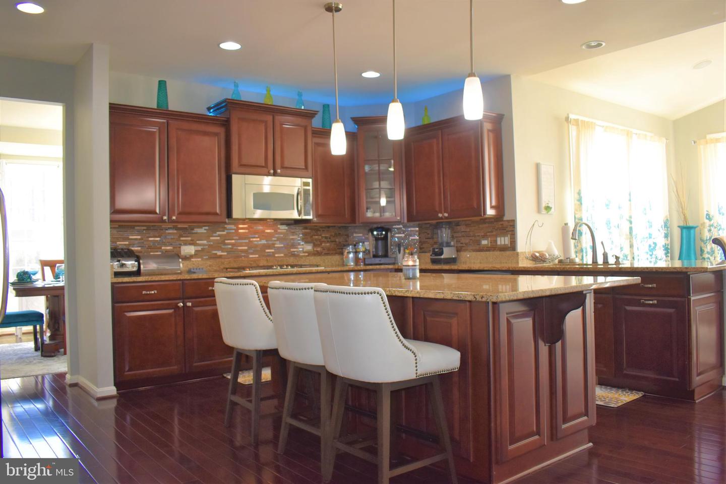 Kitchen with cherry cabinets, a large granite island, and three white bar stools.