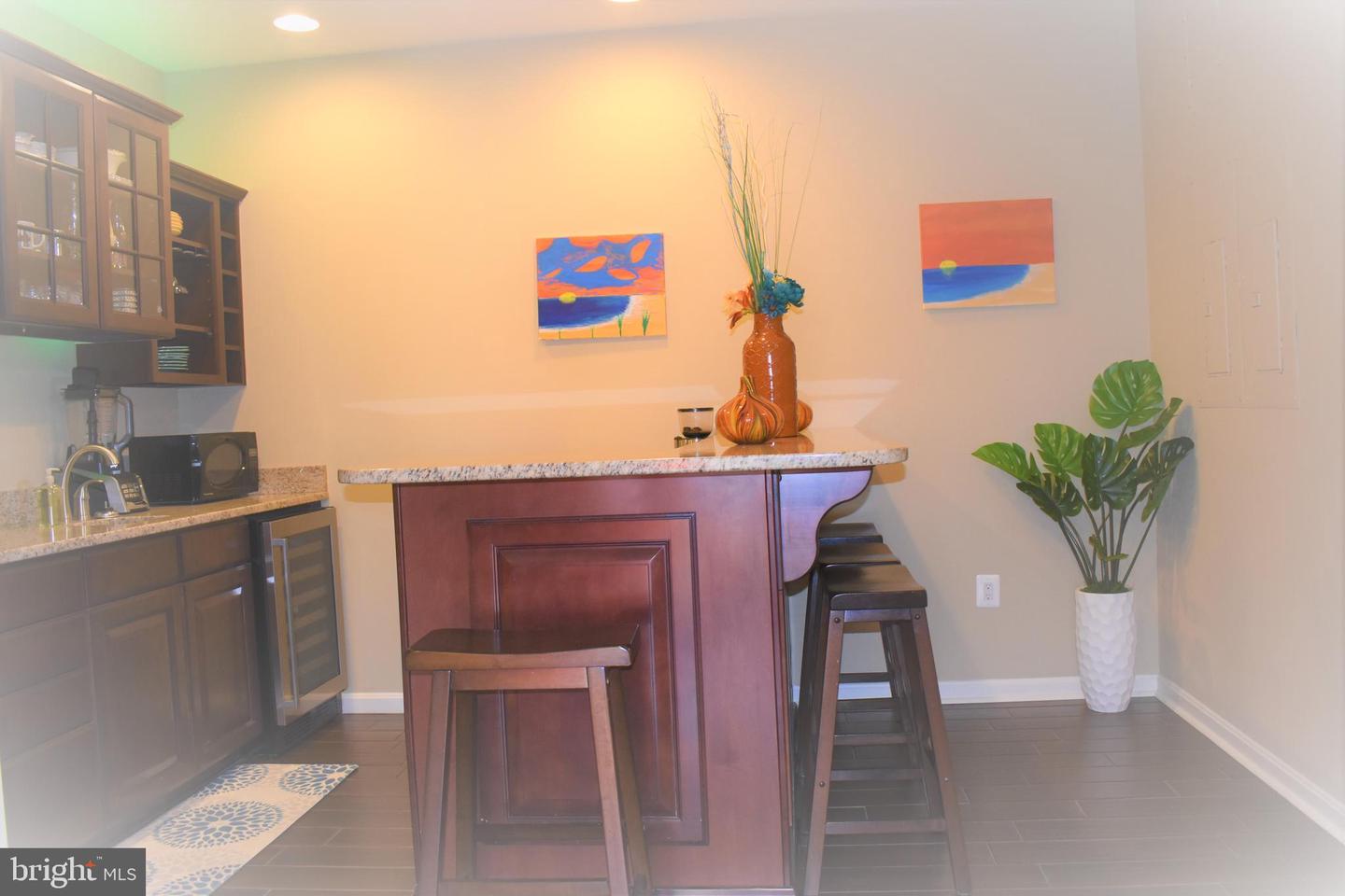 Wet bar with dark wood cabinetry, granite counter, bar stools, and colorful wall art.