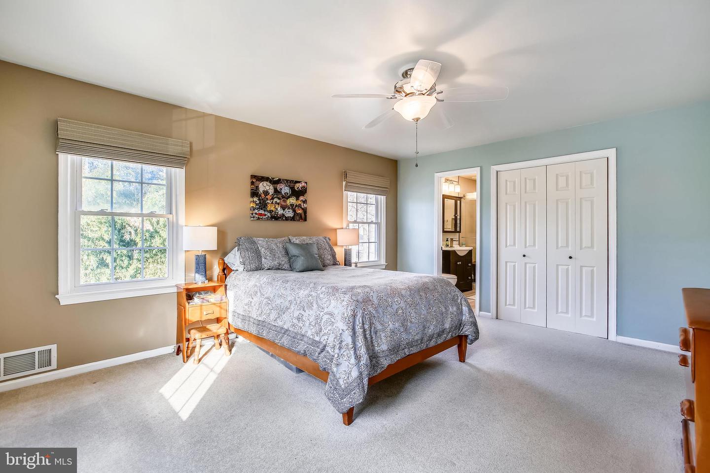 Furnished bedroom with a large bed between two windows and an open doorway to the bathroom.