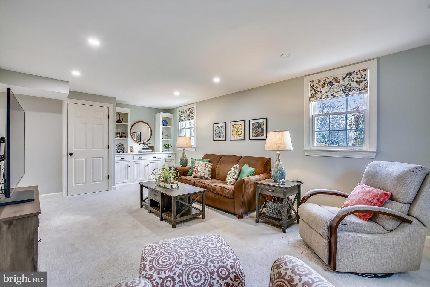 Living room with a brown sofa, gray armchair, built-in shelving, and patterned window shades.