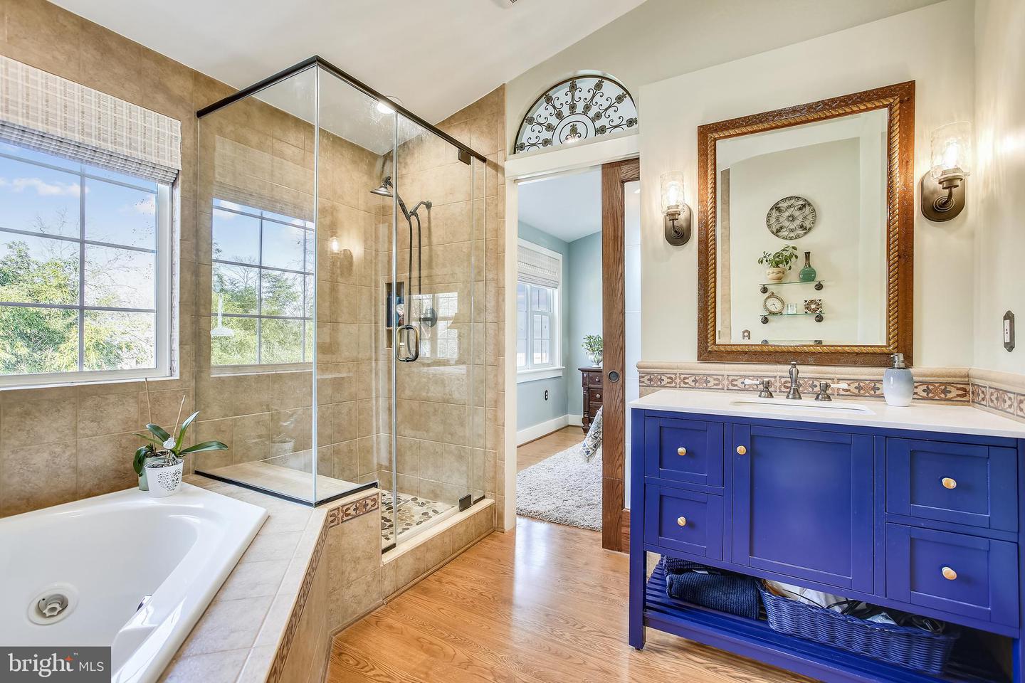 Bathroom with a glass-enclosed tiled shower, soaking tub, and deep blue vanity.