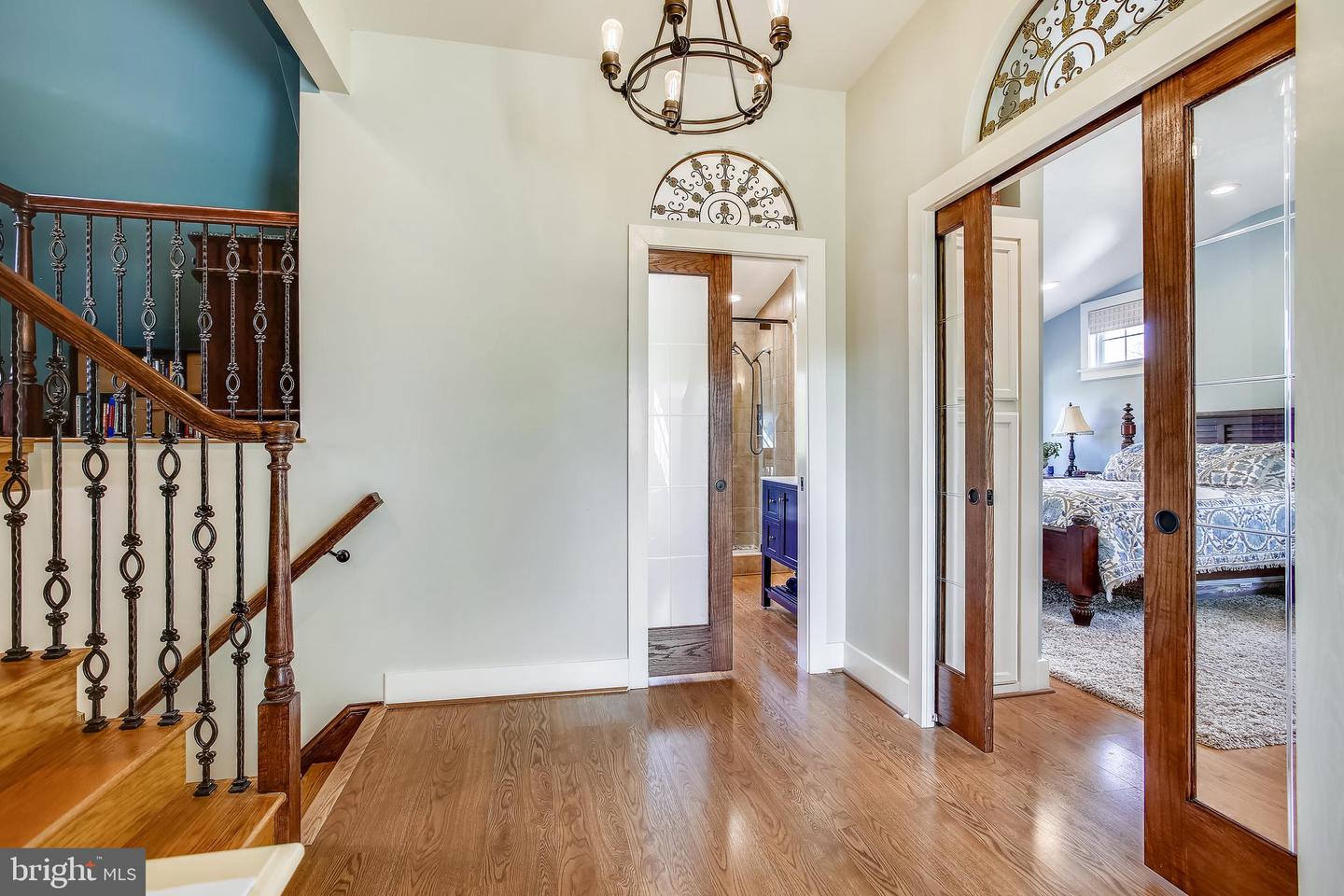 Entry hall with hardwood floors, ornate staircase, and glass doors opening to a bathroom and bedroom.