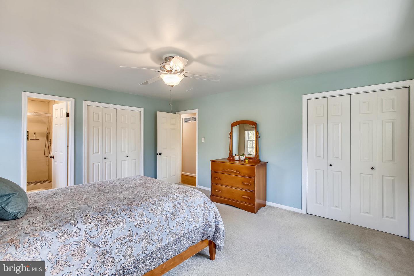 Bedroom with pale blue-green walls, patterned bedspread, wooden dresser, and ceiling fan.