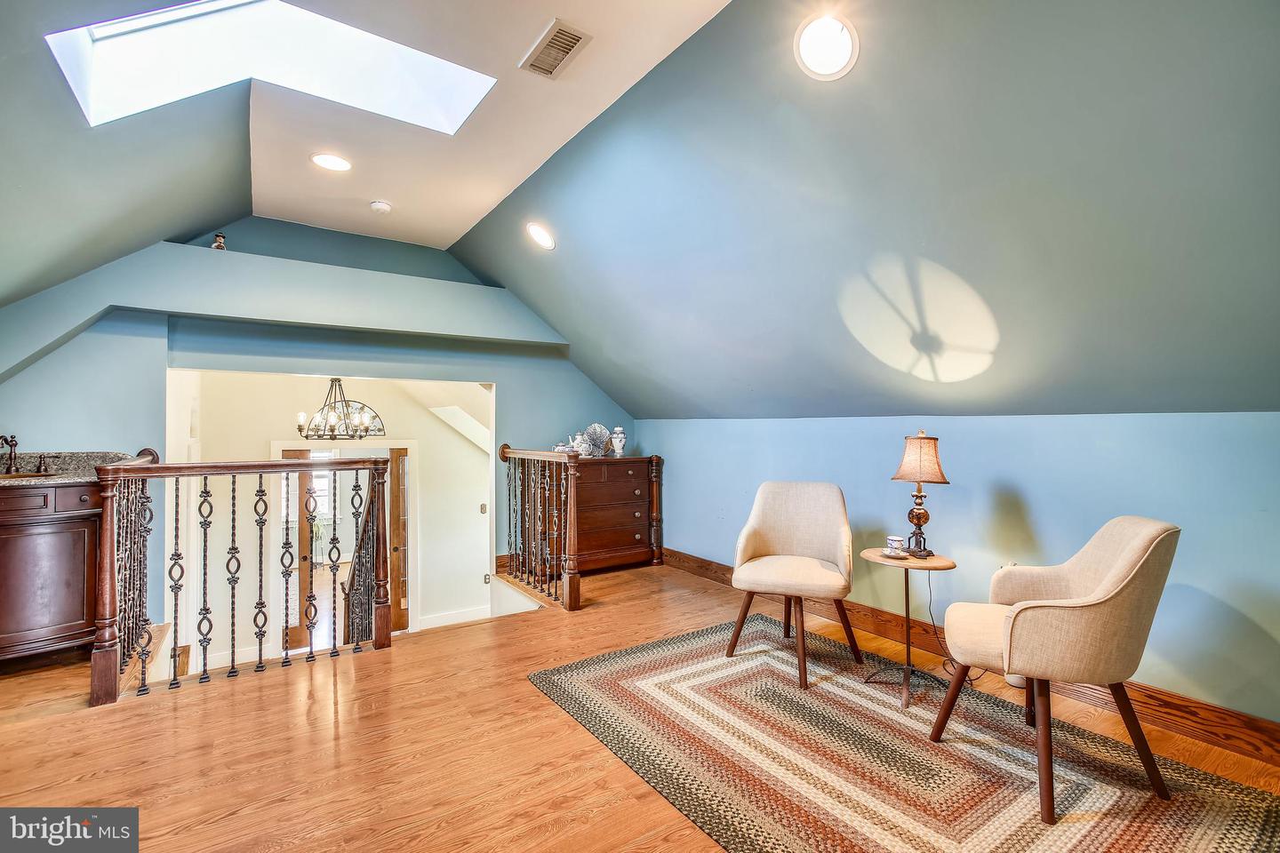 Upper-level sitting area with a skylight, vaulted ceiling, two chairs, and a decorative railing.
