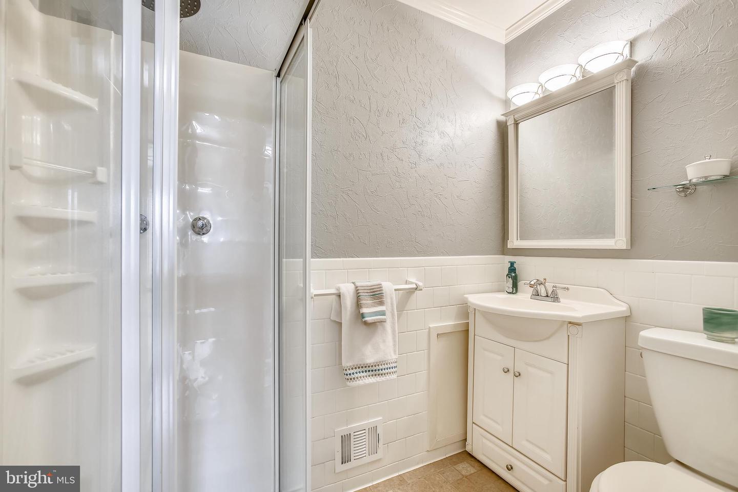 Bathroom with glass shower, white vanity and mirror, tiled walls, and towels on a rail.