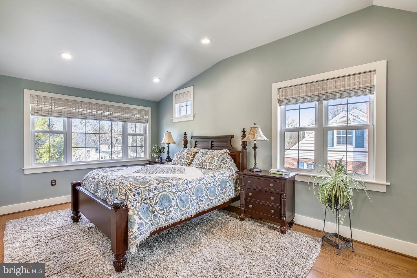 Bedroom with a dark wood four-poster bed, patterned bedding, large windows, and hardwood floors.