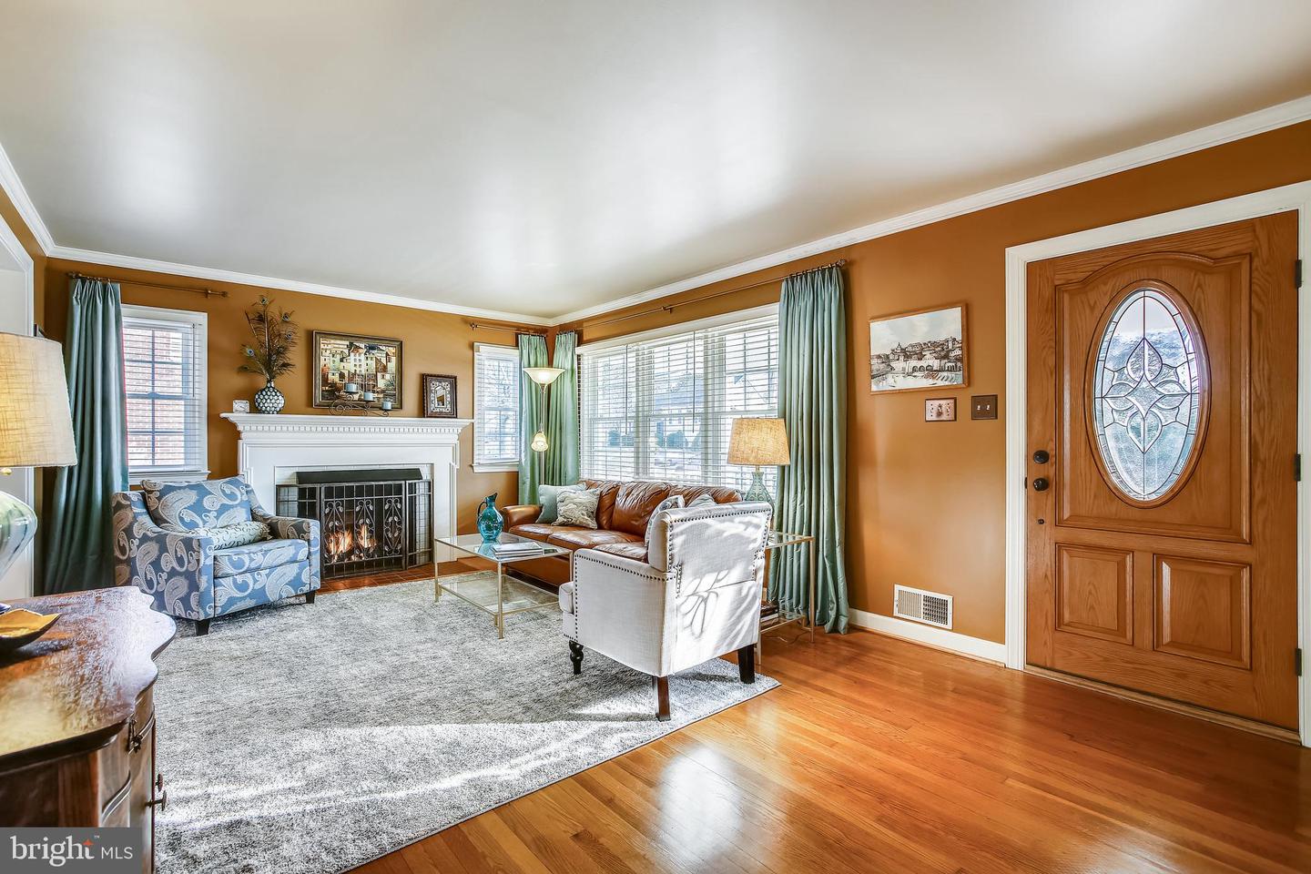 Living room with a white fireplace, brown leather sofa, and wooden front door with oval glass.