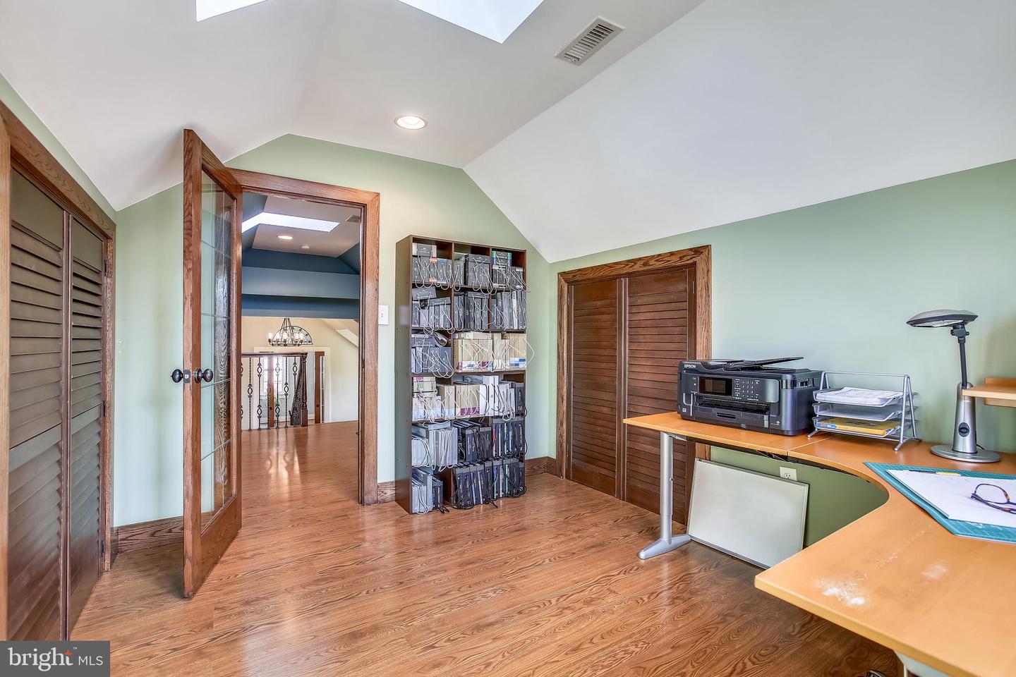Home office with sloped ceiling, wood floors, green walls, and a desk with printer.