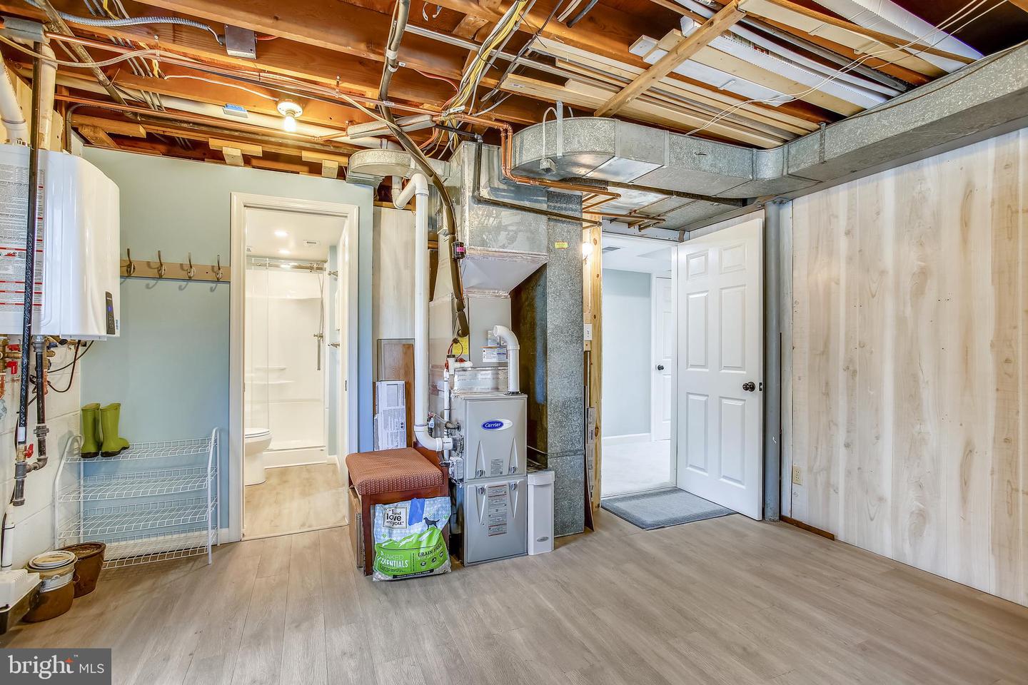 Basement utility room with exposed ceiling joists, ductwork, and a furnace beside a bathroom doorway.