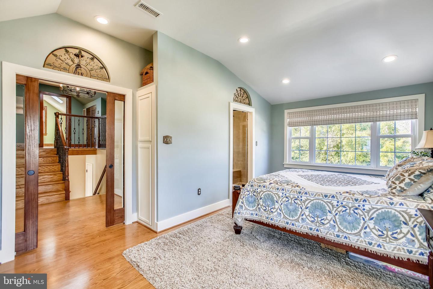 Bedroom with patterned bed, large window, vaulted ceiling, and a view of the staircase.