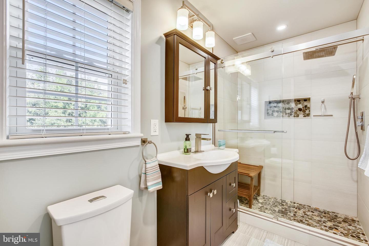 Bathroom with dark wood vanity and glass shower featuring a pebble-stone floor.