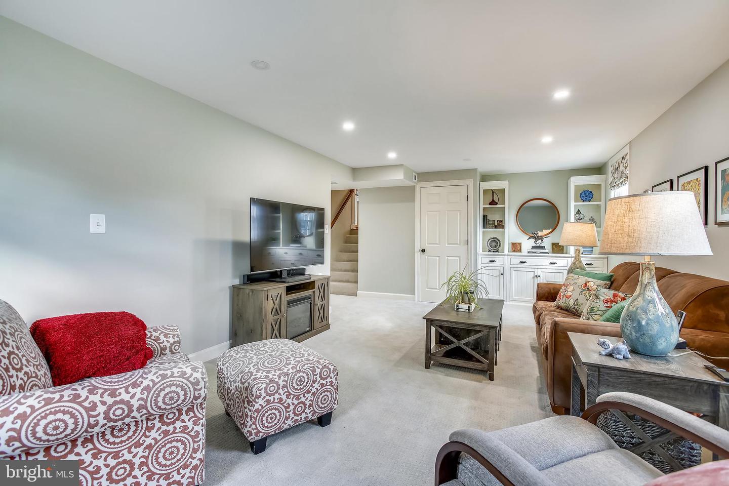 Furnished living room with patterned armchairs, a brown leather sofa, and white built-in cabinets.