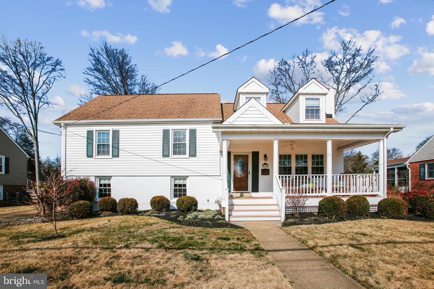 White-sided house with a covered front porch, two dormers, and a walkway across the lawn.
