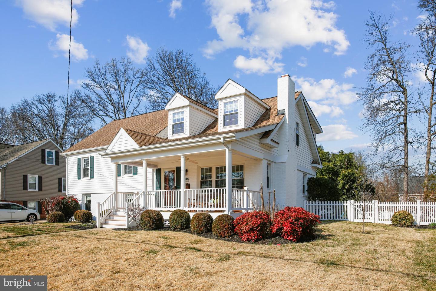 White two-story house with a covered porch, dormer windows, and white picket fence.