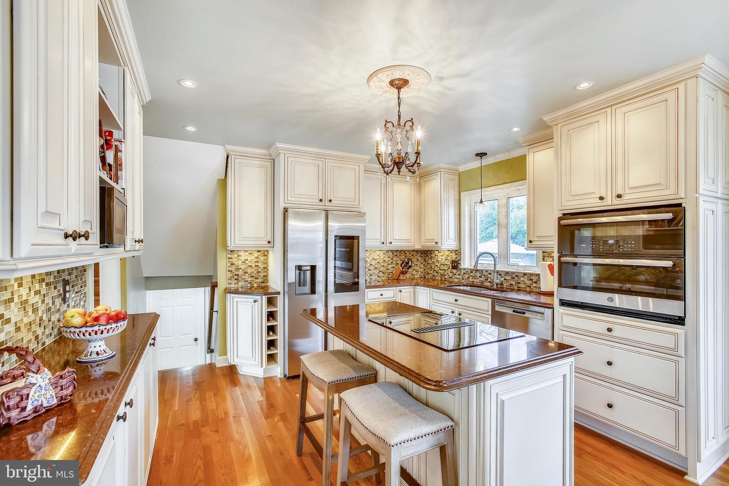Kitchen with white cabinetry, stainless appliances, mosaic backsplash, and a large stone island.