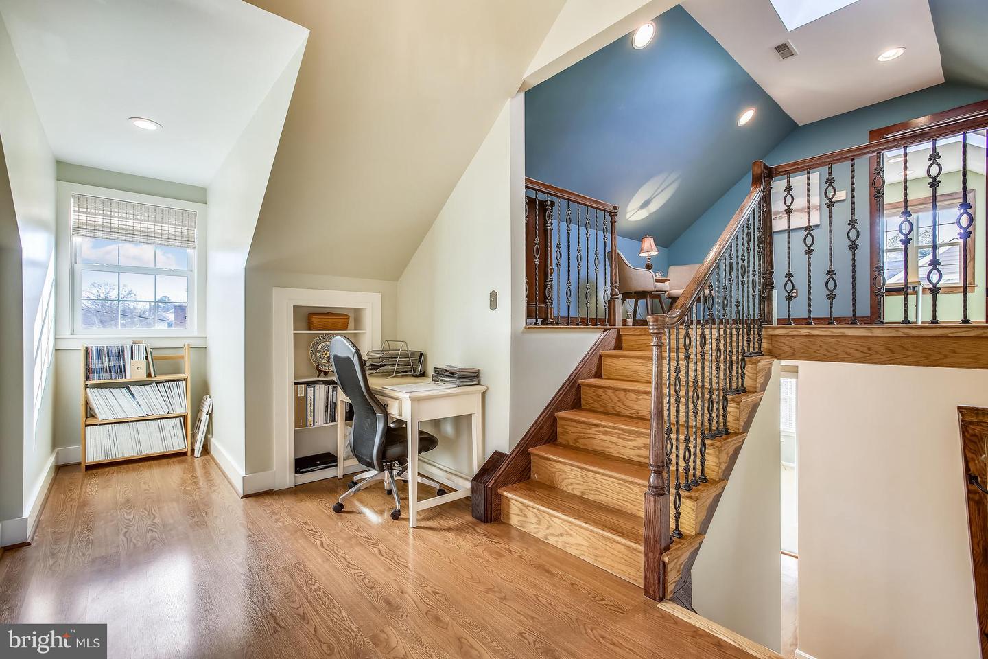 Upstairs landing with a desk and bookshelves beside a wooden staircase with dark metal railings.