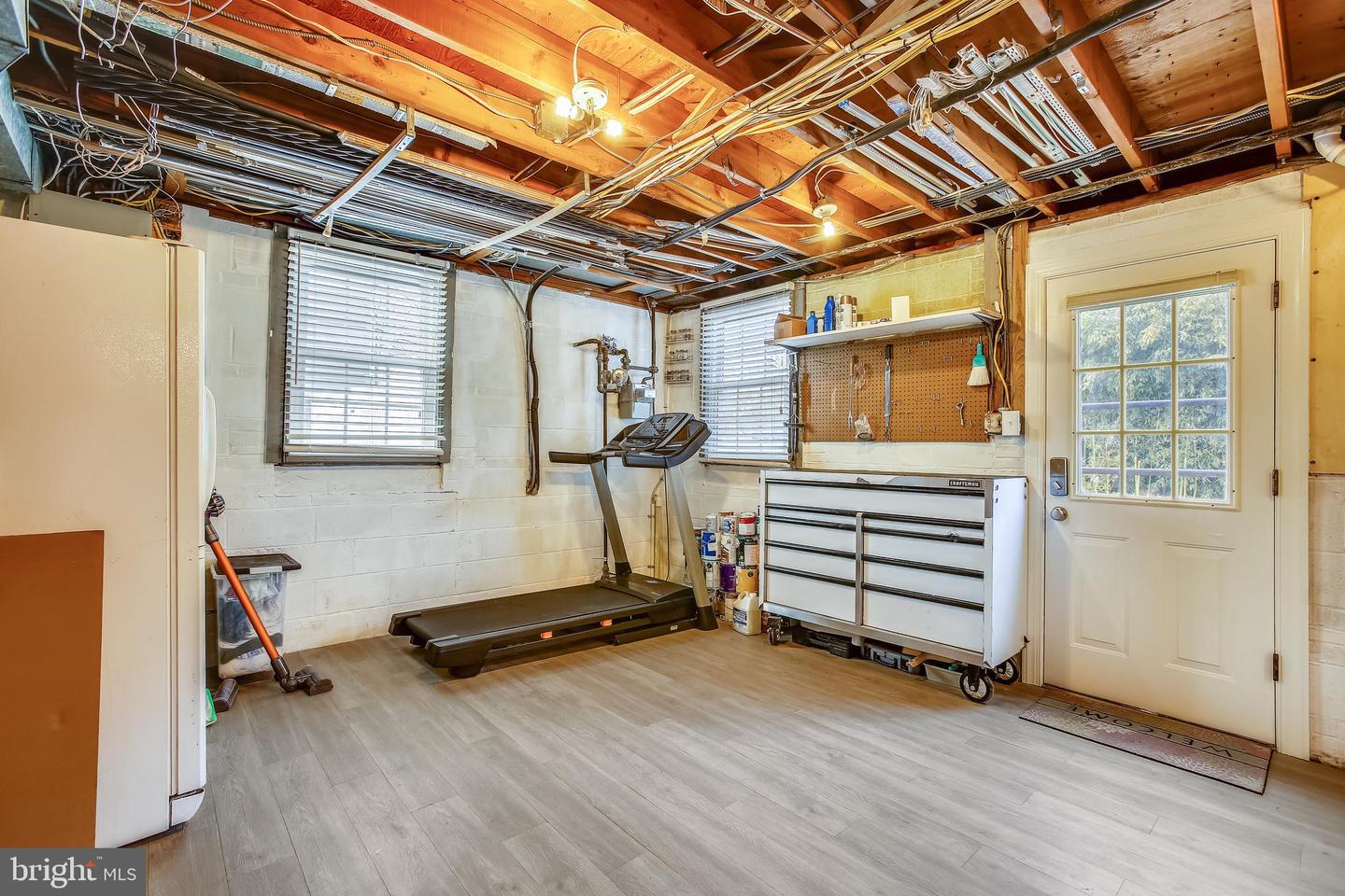 Garage with a treadmill and rolling tool chest beneath exposed ceiling joists.